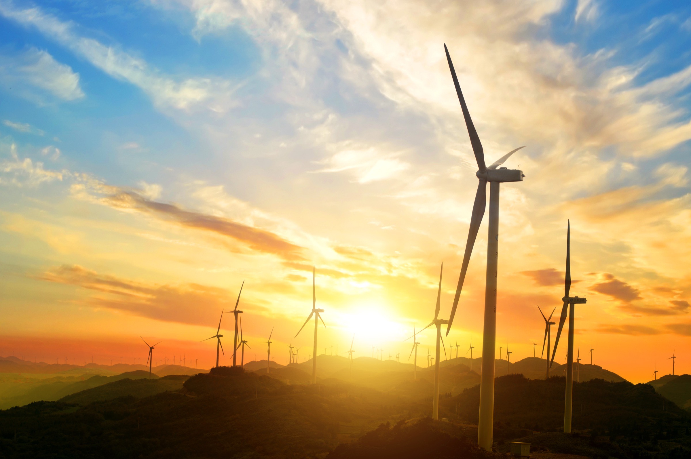 Wind turbines across a hillside at sunset